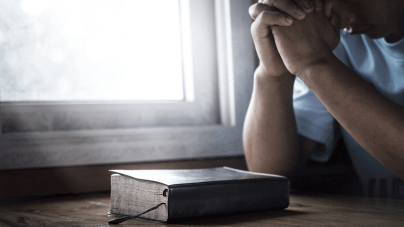 Man praying next to window